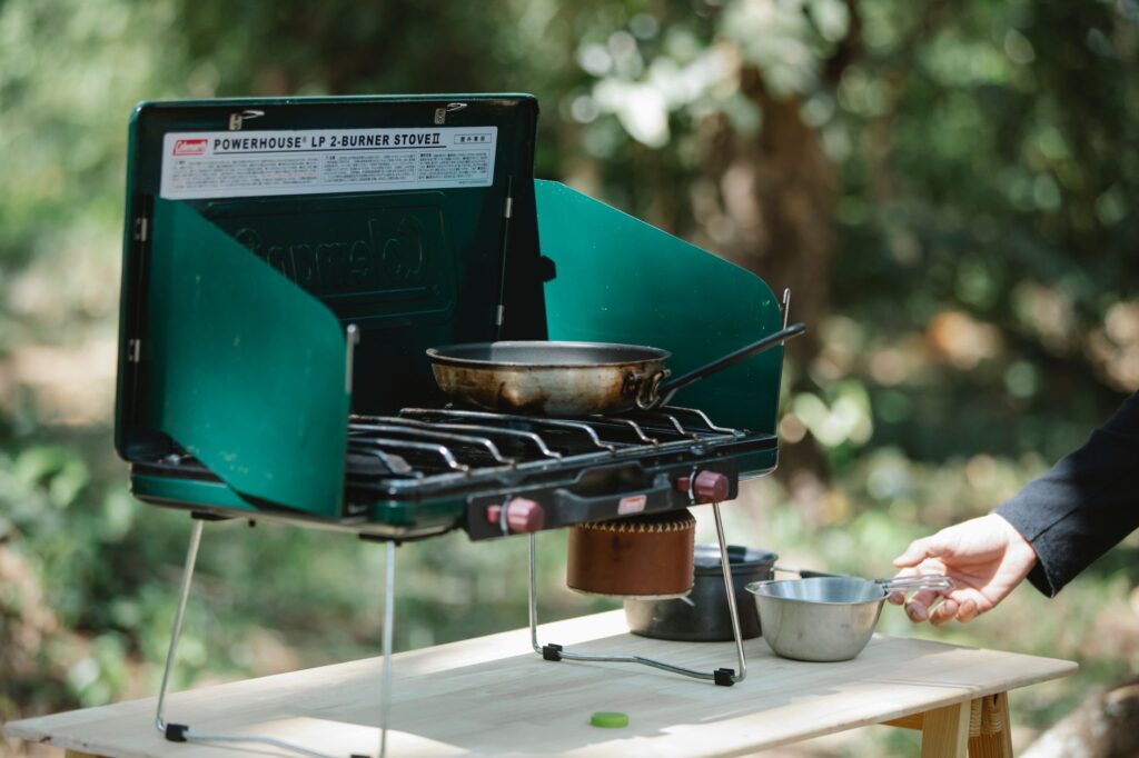 Crop unrecognizable male cooking on modern metal burner stove using skillet in forest
