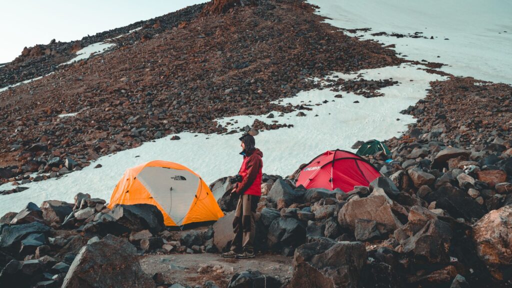 A person stands by colorful tents in a snowy mountain terrain, capturing the spirit of adventure.